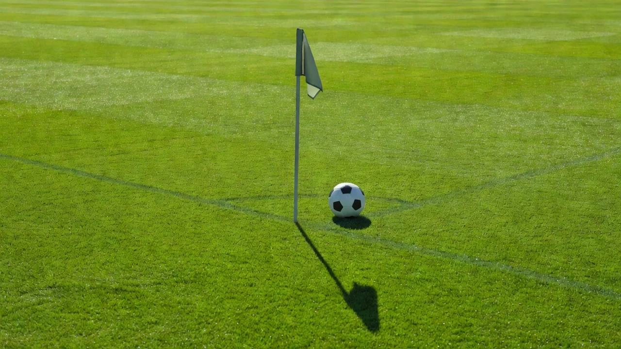 Corner flag casting a long shadow on vivid grass with a soccer ball