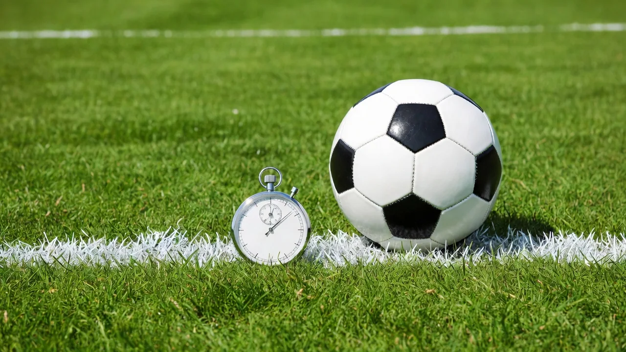 Stopwatch lying beside a soccer ball on a bright pitch line