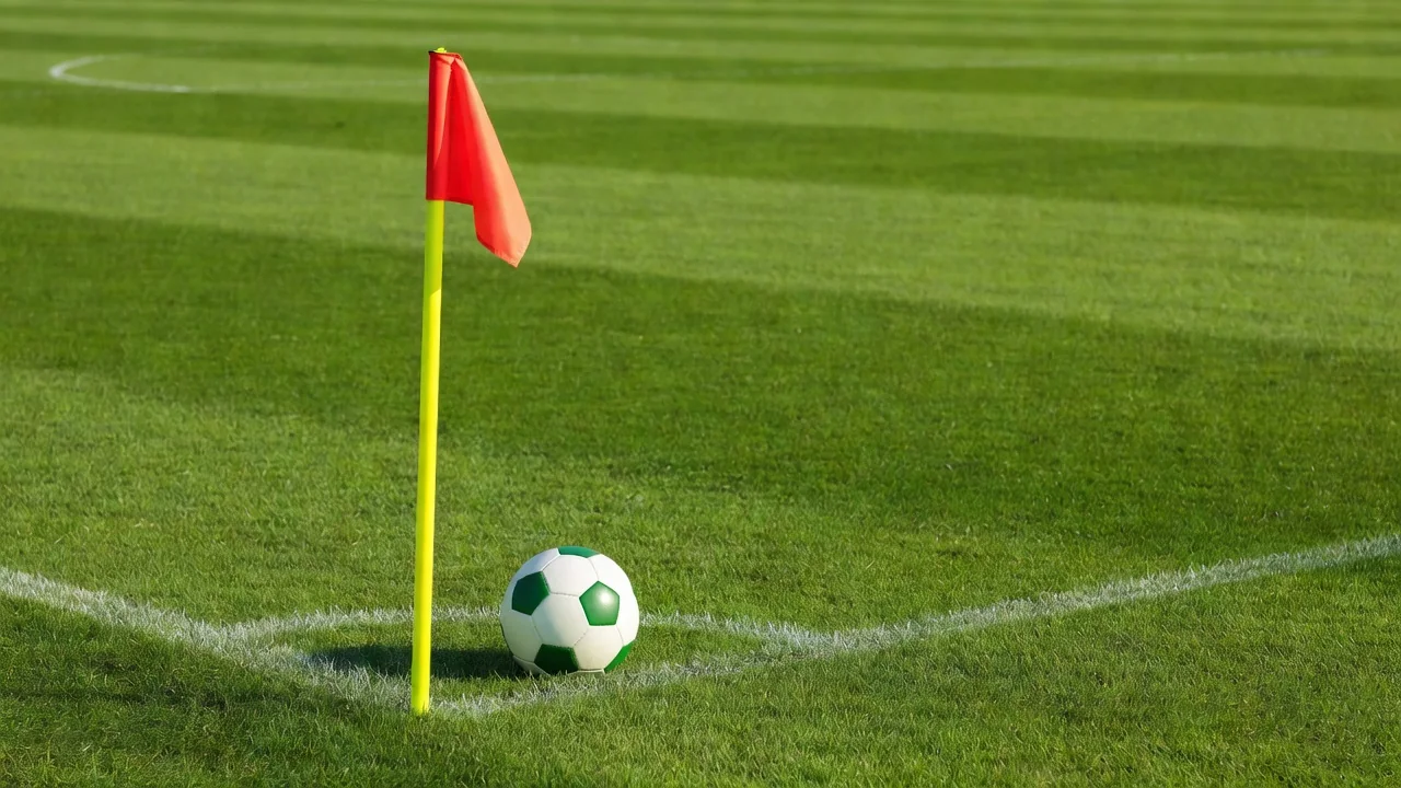 Green soccer ball beside a vivid corner flag on a bright pitch
